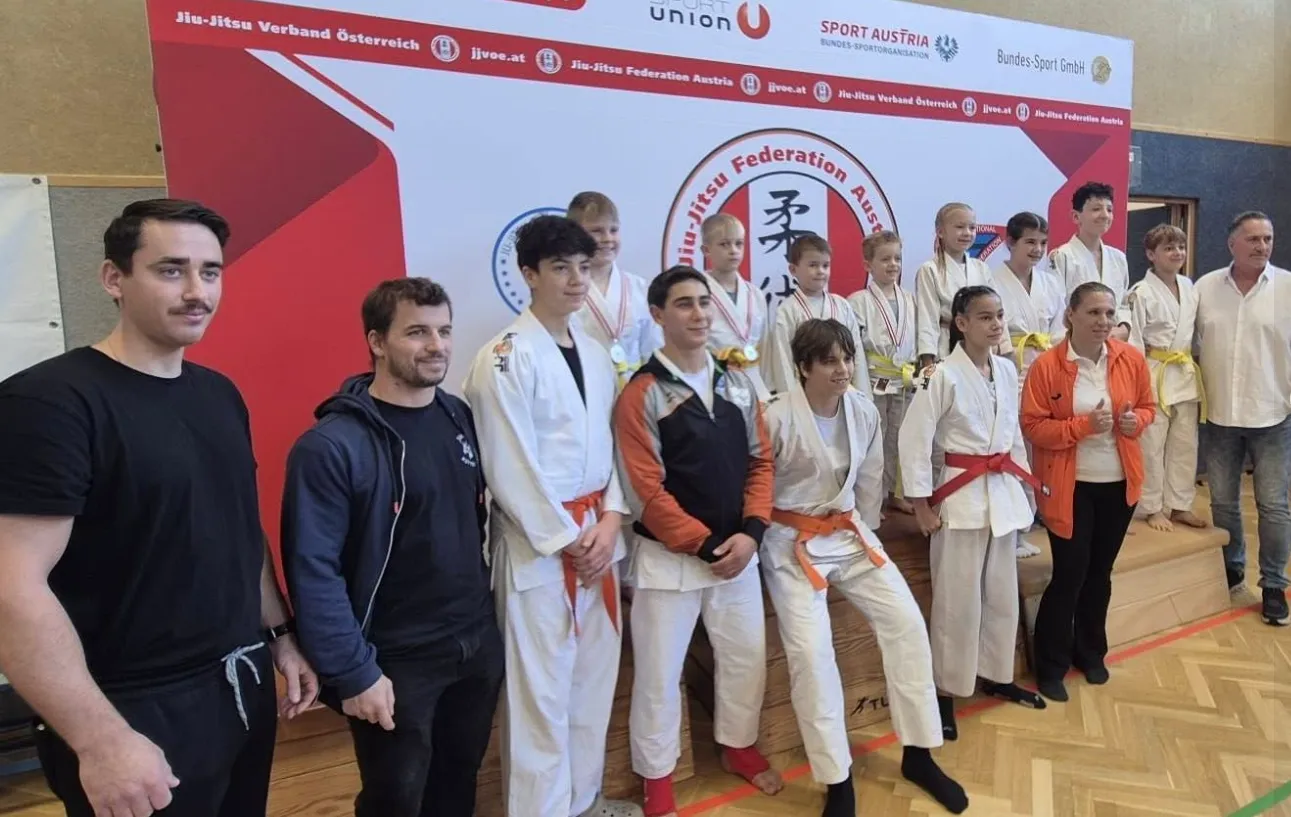 Das JJSK-Team mit Medaillen vor der Wand des Jiu-Jitsu-Verbands Österreich